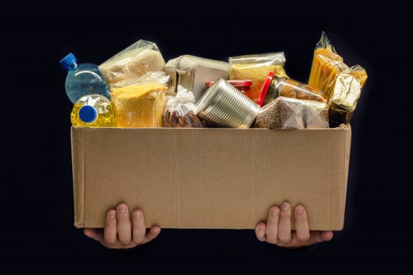 A man holding a donation box of different products on dark background